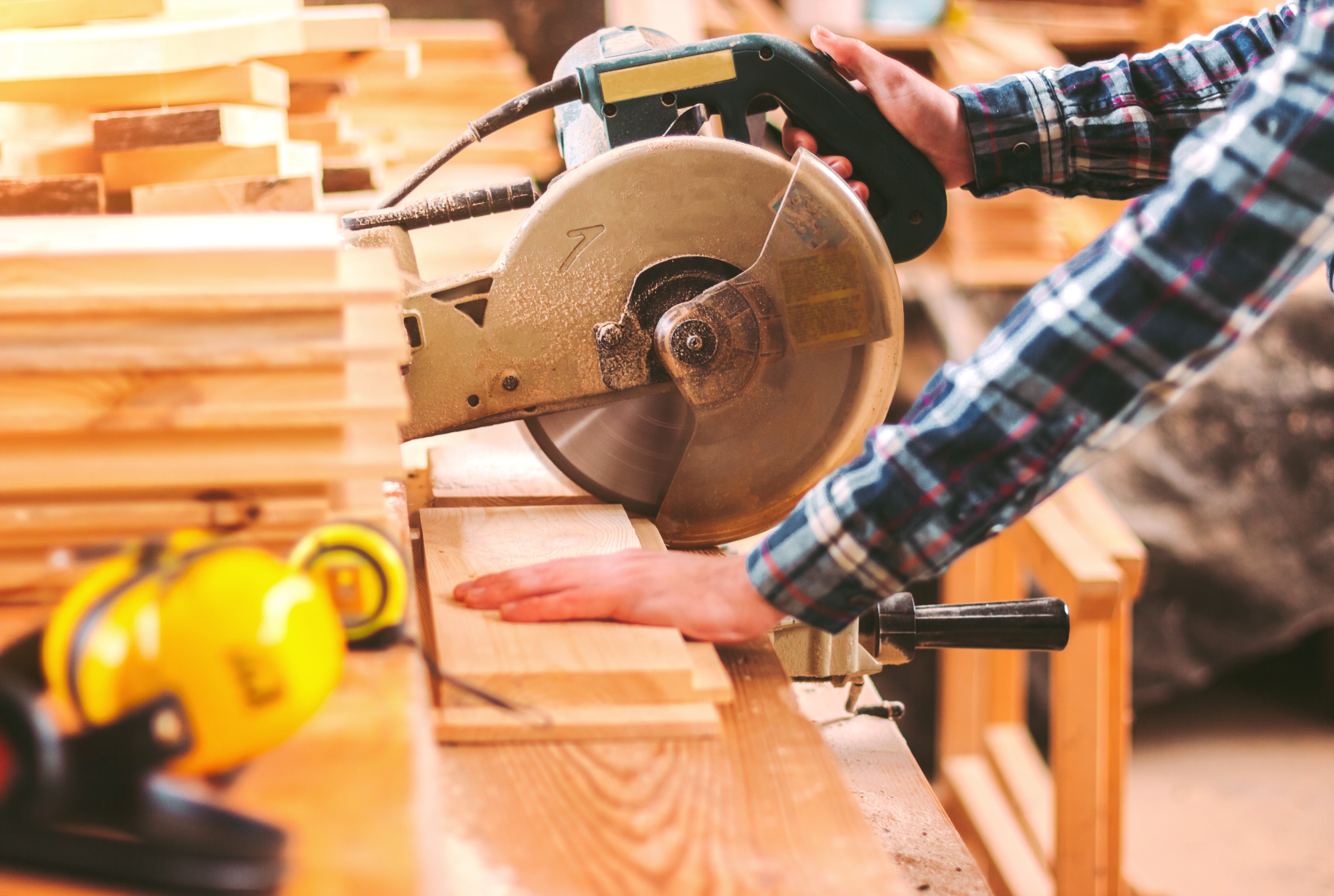 Closeup skilled cabinet maker cutting wood board with electric circular saw at woodworking sawmill. Professional cabinet maker use circular saw at sawmill factory. Wooden furniture production. Joinery