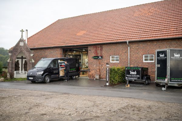 Ein Paketwagen und Anhänger vor einer Backstein-Gebäudefront mit offenem Tor; grauer Himmel.