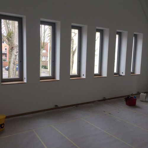 Ein leerer Raum mit sechs schmalen Fenstern, weißen Wänden und Abdeckungen auf dem Boden.