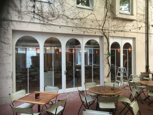 Hinterhofcafé mit leeren Tischen und Stühlen vor einem Gebäude, Kletterpflanzen an der Wand.