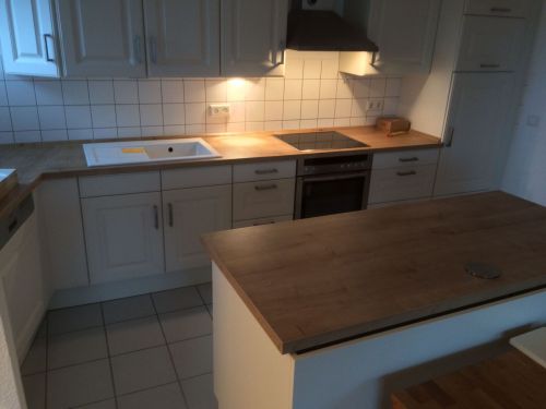 Moderne Küche mit weißen Schränken, Holzarbeitsplatten und eingebautem Herd in warmem Licht.