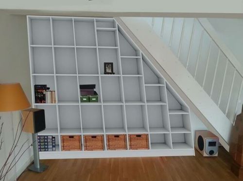 Weiße Regalwand unter Treppenschräge, mit Körben, Büchern, Lampe und Lautsprecher auf Holzboden.
