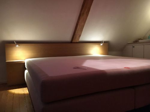 Ein gemütliches Bett in einem Dachzimmer mit Holzdecke und warmem Licht.