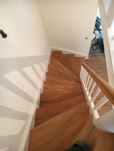 Holztreppe mit weißen Wänden und Geländer, von oben fotografiert, Schuhe sichtbar.